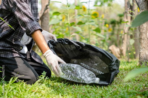 hands pick up plastic bottles, put garbage in black garbage bags to clean up at parks, avoid pollution, and be friendly to the environment and ecosystem