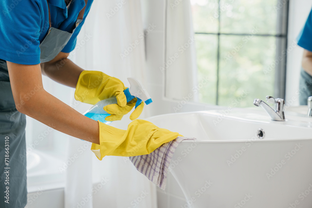 A maid wearing gloves diligently cleans bathroom sink and faucet eliminating limescale with spray detergent. Her focus on housework ensures purity hygiene and shining fixtures. spray cleaner A maid wearing gloves diligently cleans bathroom sink and faucet eliminating limescale with spray detergent. Her focus on housework ensures purity hygiene and shining fixtures. spray cleaner