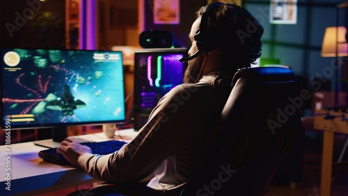 Man at home playing singleplayer videogame with spaceship shooting laser beams at asteroids, panning shot. Pro gamer destroying enemies in science fiction game using gaming mouse