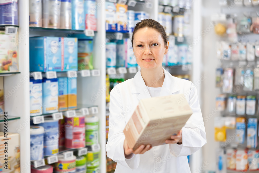 Portrait of smiling female pharmacist in sales hall of a pharmacy, demonstrating jar of baby food