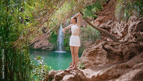 Barefoot woman stretching body on turquoise lake nature. Yoga girl warming up