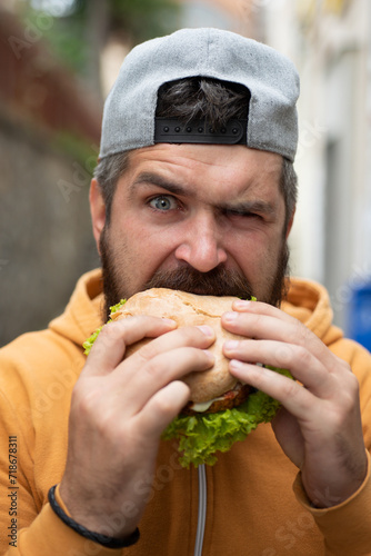 Hunger Man eat burger outdoor. Man eat tasty Hamburger on street. Burger on lunch. Cheeseburger or hamburger. Man eating tasty burgers outside. Tasty burger. Bearded man enjoying delicious burger.