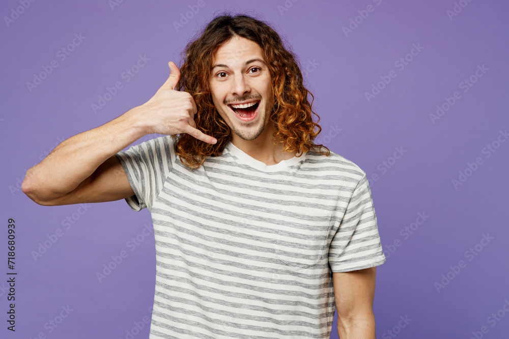 Young smiling cheerful man he wears grey striped t-shirt casual clothes doing phone gesture like says call me back isolated on plain pastel light purple background studio portrait. Lifestyle concept. Young smiling cheerful man he wears grey striped t-shirt casual clothes doing phone gesture like says call me back isolated on plain pastel light purple background studio portrait. Lifestyle concept.