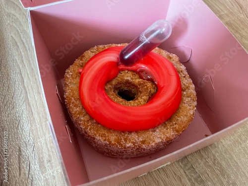 Cronut - a donut made from croissant dough - with pink fruit topping and a vial of liqueur to fill inside. In a pink box. High quality photo