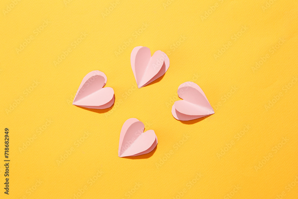 Pastel pink paper hearts are artistically arranged on a yellow background. The space is viewed from above with a women's day theme. Banner, commercial. Pastel pink paper hearts are artistically arranged on a yellow background. The space is viewed from above with a women's day theme. Banner, commercial.