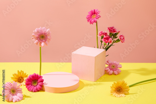Front view of two pastel pink podiums decorated with gerberas and carnations on a yellow pink background. Ideal space for product display. Women's Day theme.