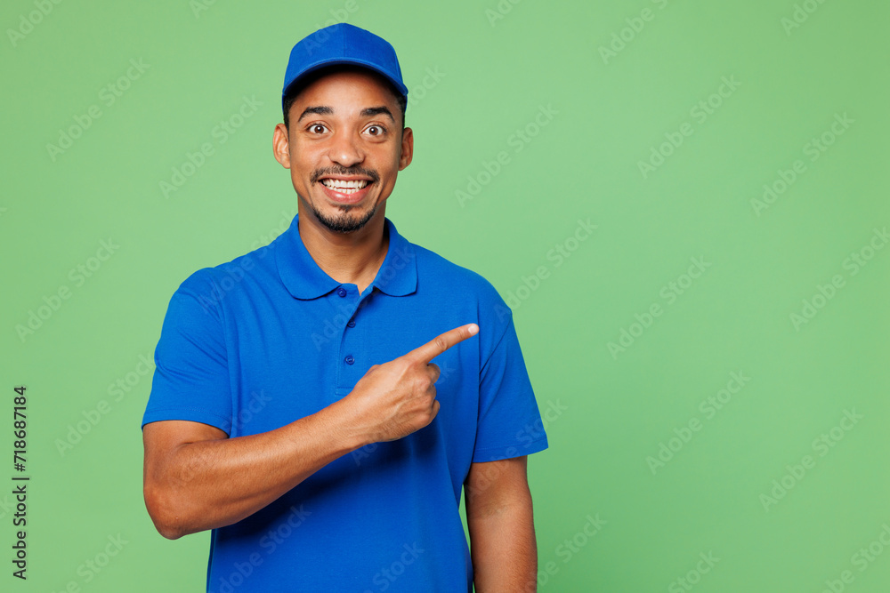 Professional delivery guy employee man he wear blue cap t-shirt uniform workwear work as dealer courier point index finger aside on area copy space isolated on plain green background. Service concept.