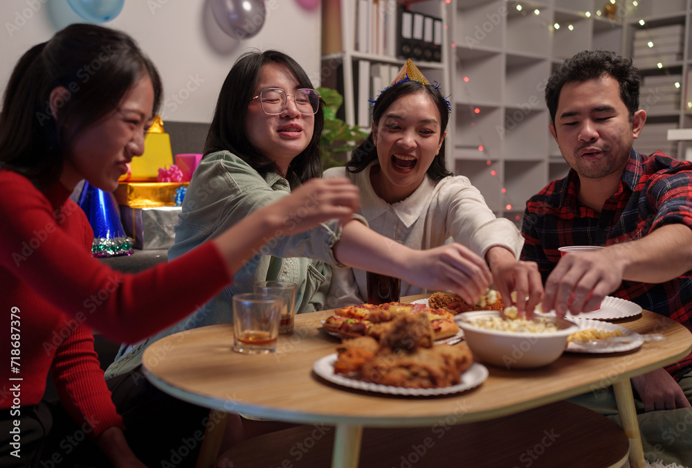 Group of happy young friends celebrating at a party with snacks popcorn pizza and drinks. The atmosphere at the event was full of laughter while sitting at the dining table together in the home office