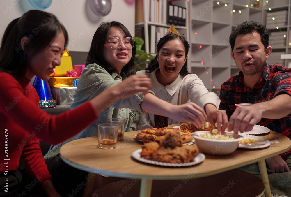 Group of happy young friends celebrating at a party with snacks popcorn pizza and drinks. The atmosphere at the event was full of laughter while sitting at the dining table together in the home office Group of happy young friends celebrating at a party with snacks popcorn pizza and drinks. The atmosphere at the event was full of laughter while sitting at the dining table together in the home office