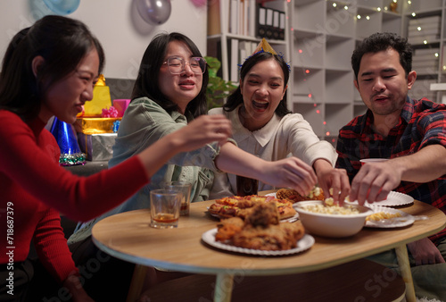 Group of happy young friends celebrating at a party with snacks popcorn pizza and drinks. The atmosphere at the event was full of laughter while sitting at the dining table together in the home office © Phimwilai