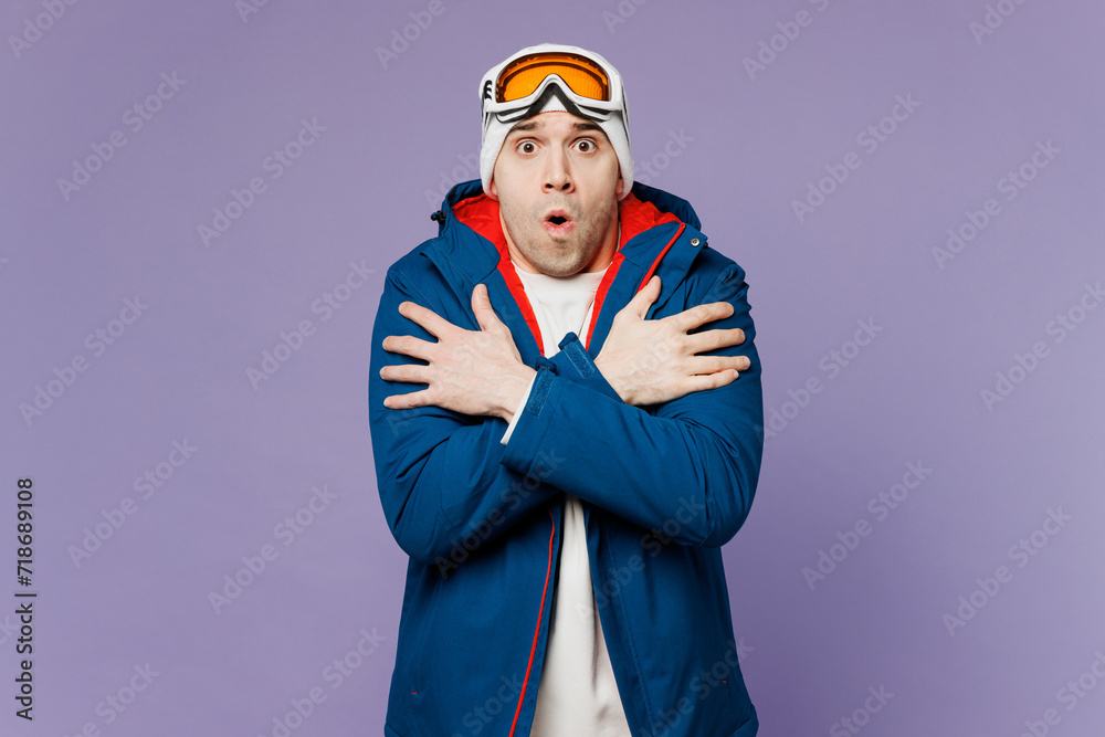 Fototapeta premium Skier freezing sad shocked man wears blue windbreaker jacket ski goggles mask warming hug himself spend extreme weekend winter season in mountains isolated on plain purple background. Hobby concept.