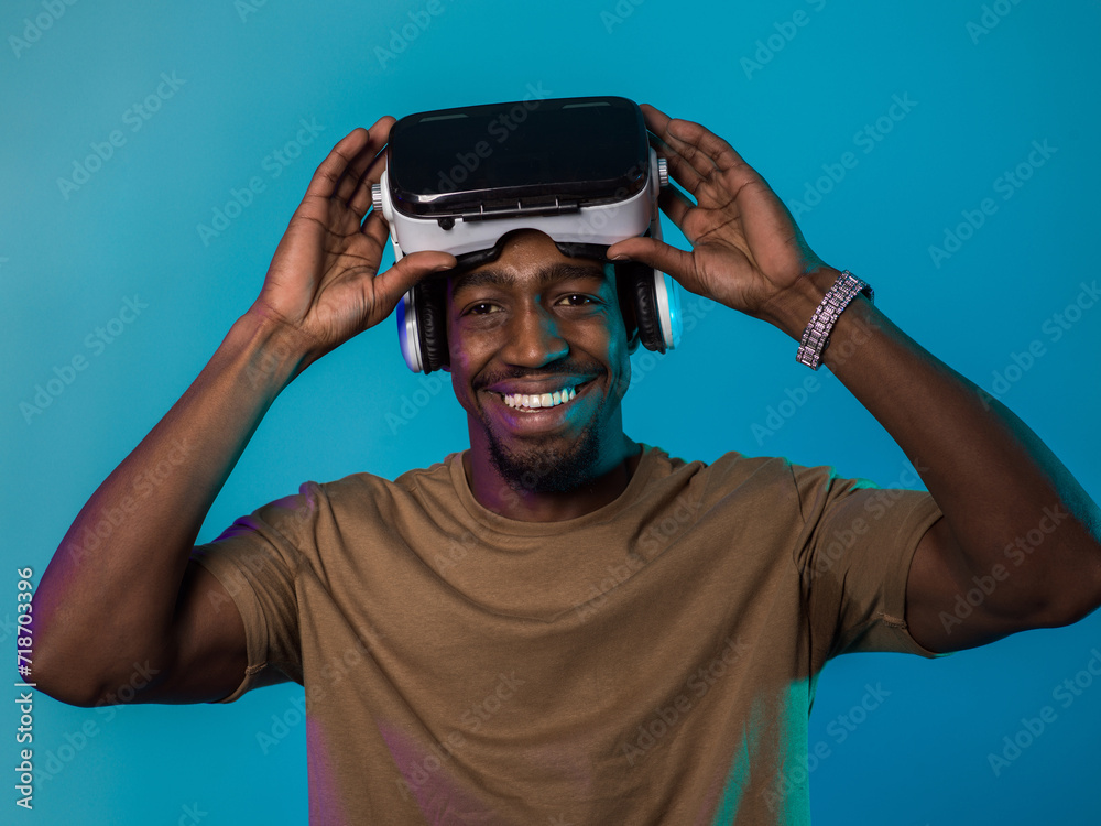 In a futuristic visual, an African American man stands isolated against a striking blue backdrop, adorned with VR glasses that transport him into a cutting-edge virtual reality experience, merging In a futuristic visual, an African American man stands isolated against a striking blue backdrop, adorned with VR glasses that transport him into a cutting-edge virtual reality experience, merging