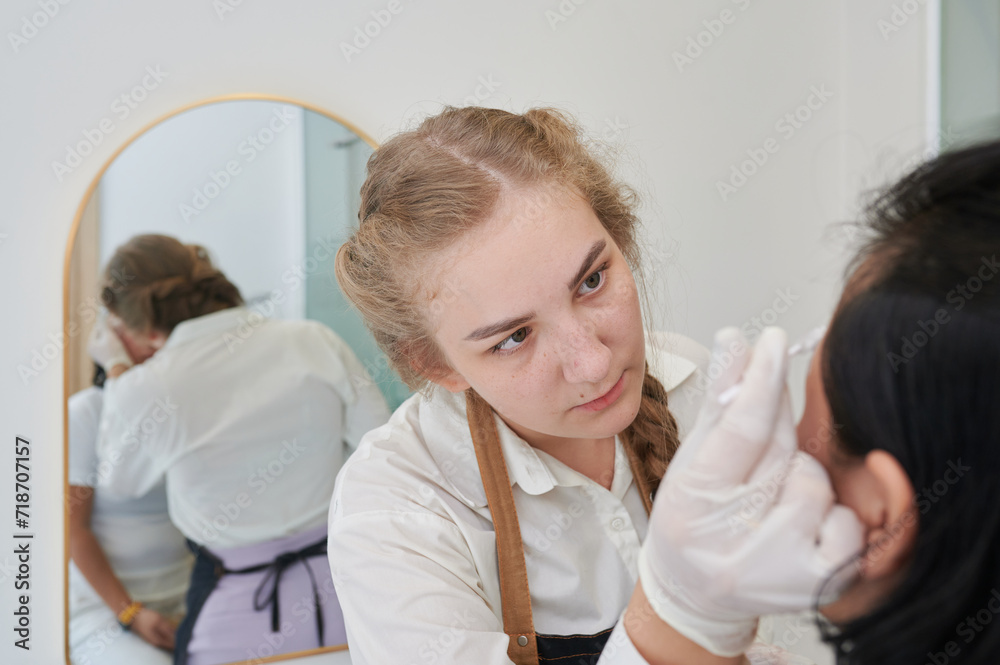 Fototapeta premium Young Asian woman undergoing eyebrow correction procedure in beauty salon, closeup