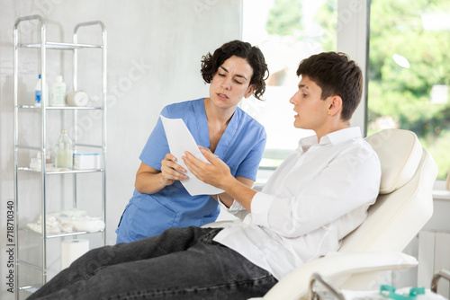 Young brunette man talking with female doctor while reading and signing of health conract