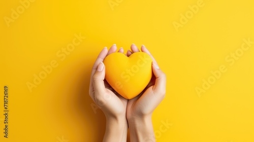 Female hands on a yellow background holding a yellow heart. The concept of donations and family insurance, World Heart Day. Valentine's Day. photo