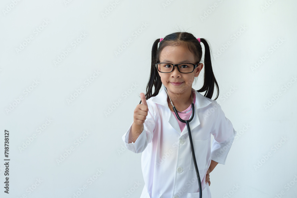 A girl wearing a doctor's uniform, standing with smiling glasses and a stethoscope is playing a doctor. and give a thumbs up showing excellent work, excellent, on a white background. A girl wearing a doctor's uniform, standing with smiling glasses and a stethoscope is playing a doctor. and give a thumbs up showing excellent work, excellent, on a white background.