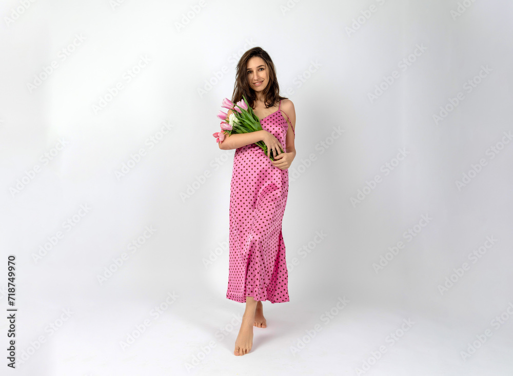 beautiful woman in pink polka dot dress with tulip flowers in hand on cyclorama in studio. celebrating international women's day, March 8th. smiling fit girl ready for spring beautiful woman in pink polka dot dress with tulip flowers in hand on cyclorama in studio. celebrating international women's day, March 8th. smiling fit girl ready for spring