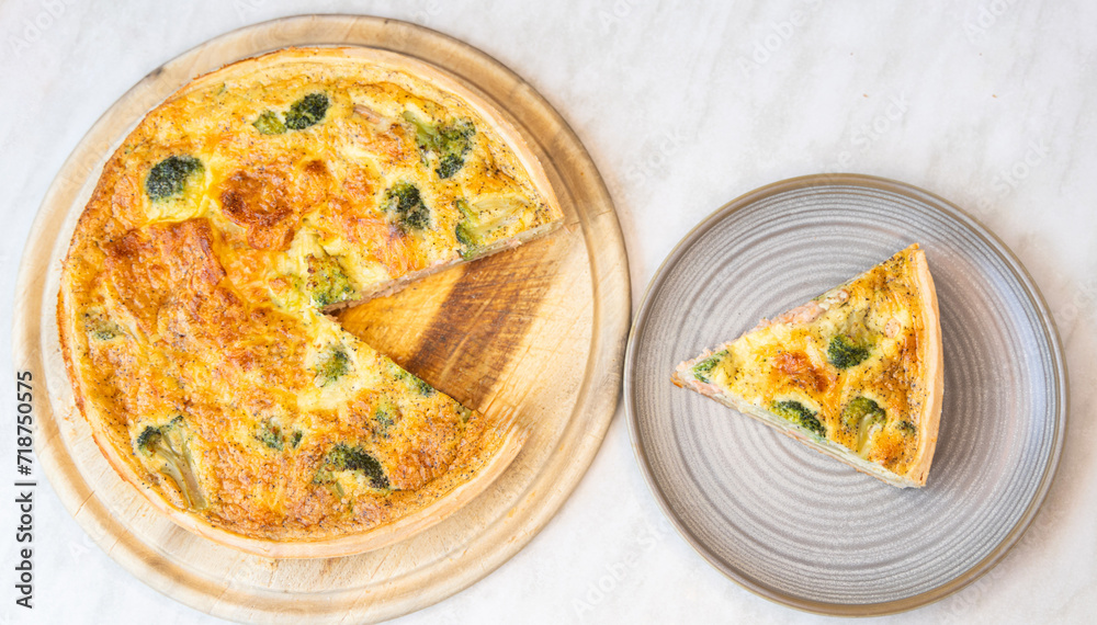 tasty broccoli and salmon pie or traditional french quiche on wooden round board.slice served on plate, section view. delicious ingredients baked on dough sheet.close up,top views