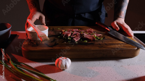 pieces of cooked and sliced meat sprinkled with fresh onions lie on a wooden board in front of the cook ready to serve. photo