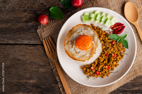 Top view of rice and fried egg topped with stir fried pork with yellow curry paste in white plate on wooden table background. 