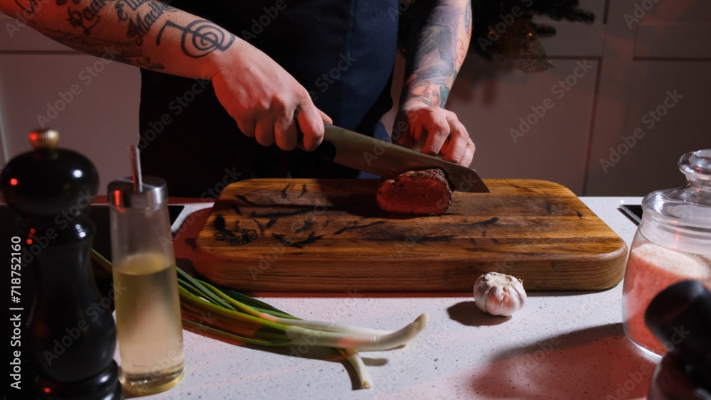 Obraz premium A cook on a wooden board cuts a fried steak into large pieces, close-up