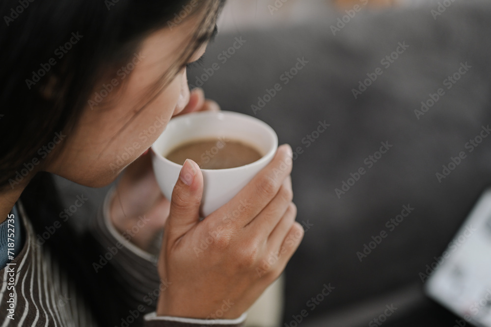 Cropped shot young woman enjoying her cup of tea or coffee while sitting on couch Cropped shot young woman enjoying her cup of tea or coffee while sitting on couch
