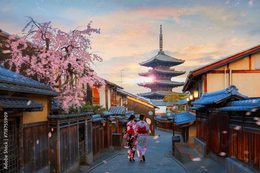 Fototapeta premium Scenic cityscape of Yasaka pagoda sunset in Kyoto with a young Japanese woman in a traditional Kimono dress during full bloom cherry blossom and scatter sakura petals