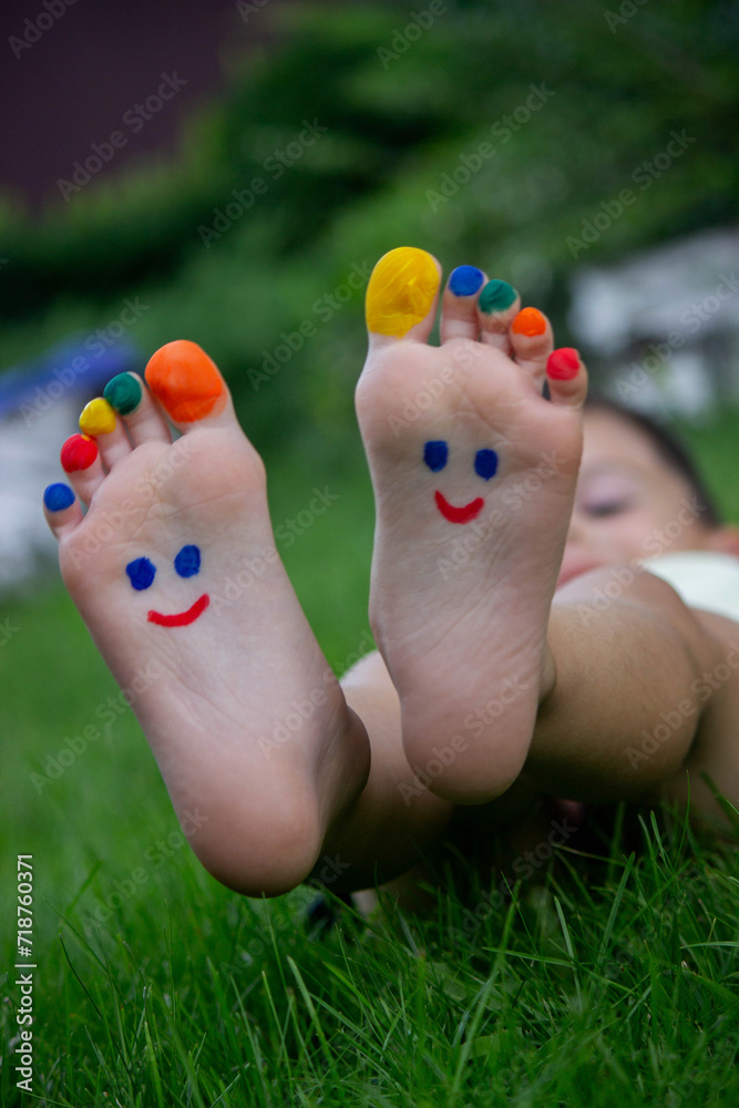 Fototapeta premium Children's legs with a pattern made of paints are smiling on the green grass