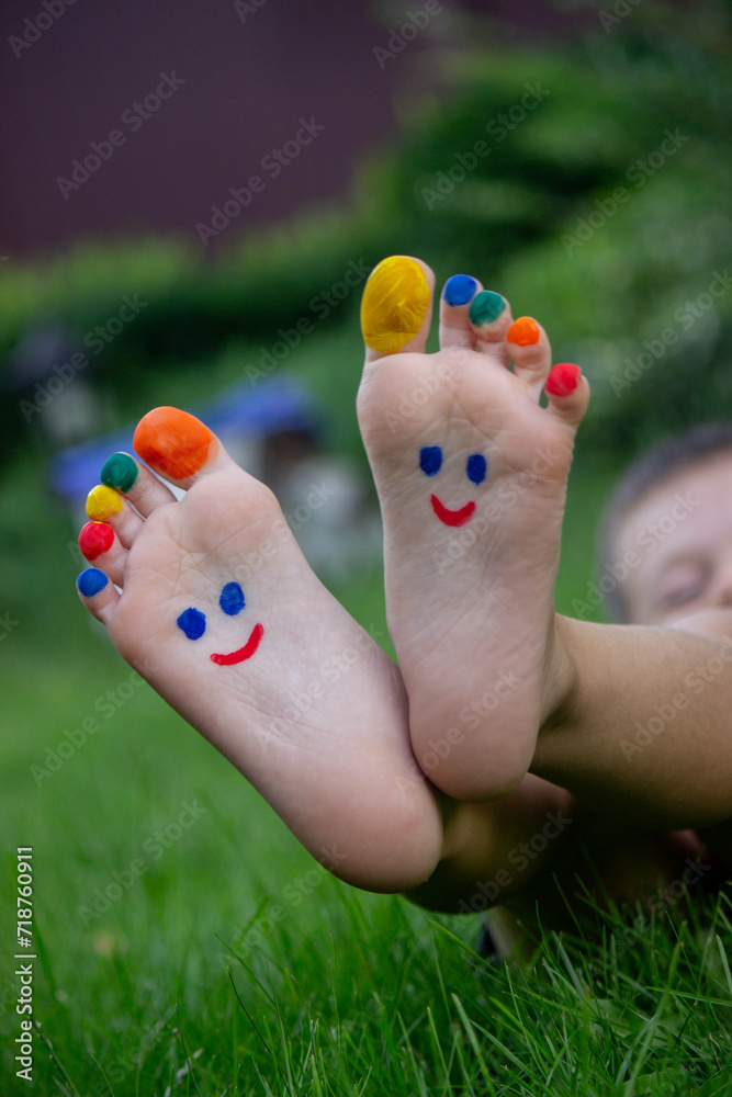 Fototapeta premium Children's legs with a pattern made of paints are smiling on the green grass