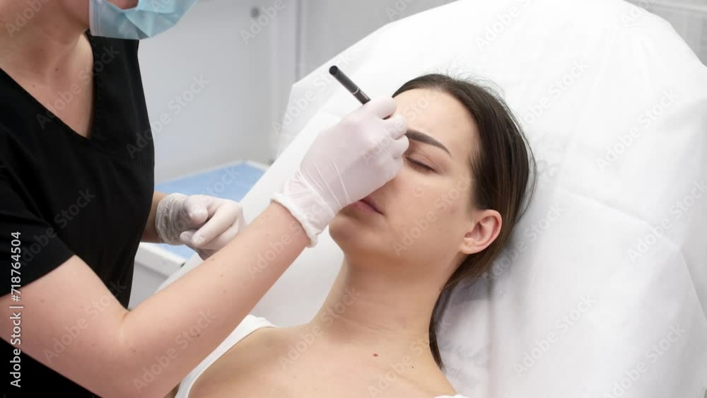 Beauticians in white gloves draw on the face with a pencil, preparing to inject a rejuvenating facial filler into a young woman. Injection beauty procedure. Beauticians in white gloves draw on the face with a pencil, preparing to inject a rejuvenating facial filler into a young woman. Injection beauty procedure.