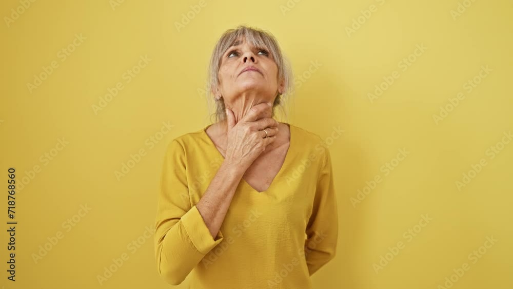 Suffering middle age woman, portrait of distress with grey hair in pony tail, battling flu symptoms, sore throat, pain in neck, feverish infection on isolated yellow background Suffering middle age woman, portrait of distress with grey hair in pony tail, battling flu symptoms, sore throat, pain in neck, feverish infection on isolated yellow background