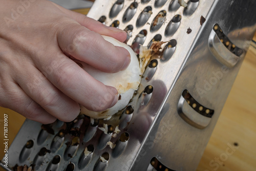 Zbliżenie na dłoń ścierającą na tarce kuchennej surowe pieczarki do farszu 