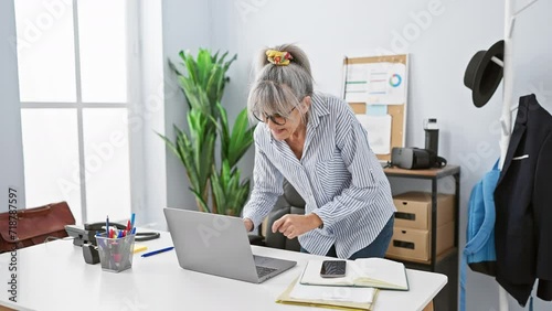 A mature woman with grey hair celebrates a success at her office workplace in front of a laptop photo