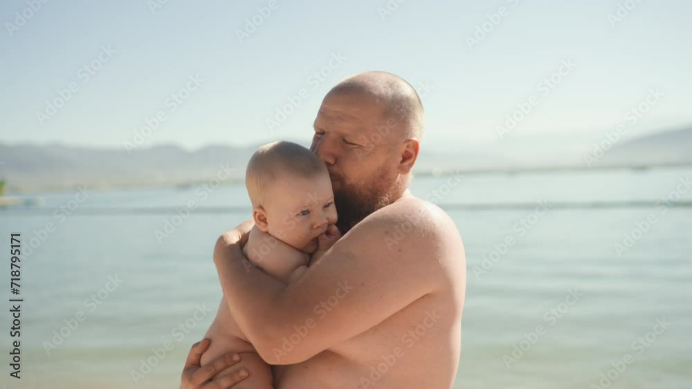 Authentic shot of young father caressing and kissing his baby standing by the sea. Dad and little boy hug during summer vacation. Concept of family, fatherhood, motherhood, parenthood, childhood, life Authentic shot of young father caressing and kissing his baby standing by the sea. Dad and little boy hug during summer vacation. Concept of family, fatherhood, motherhood, parenthood, childhood, life