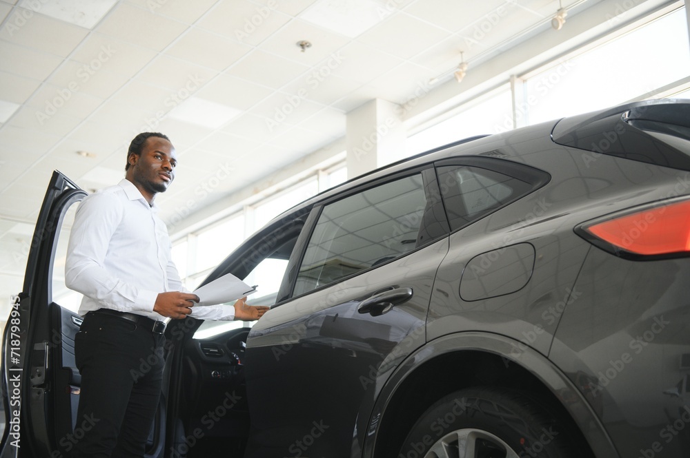 young african american car dealership principal standing in vehicle showroom