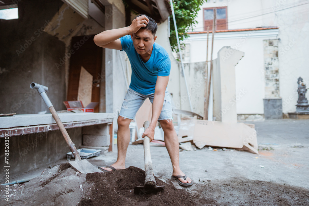 man gets headache while working on cement mixture using a hoe to build a house