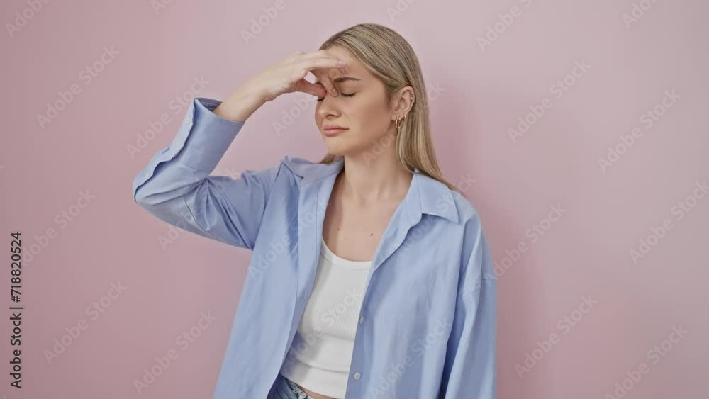 Overworked young blonde rubs tired eyes and aches head in fatigue, wearing shirt, portraits frustration against isolated pink wall. stressful health problems from work strain. Overworked young blonde rubs tired eyes and aches head in fatigue, wearing shirt, portraits frustration against isolated pink wall. stressful health problems from work strain.