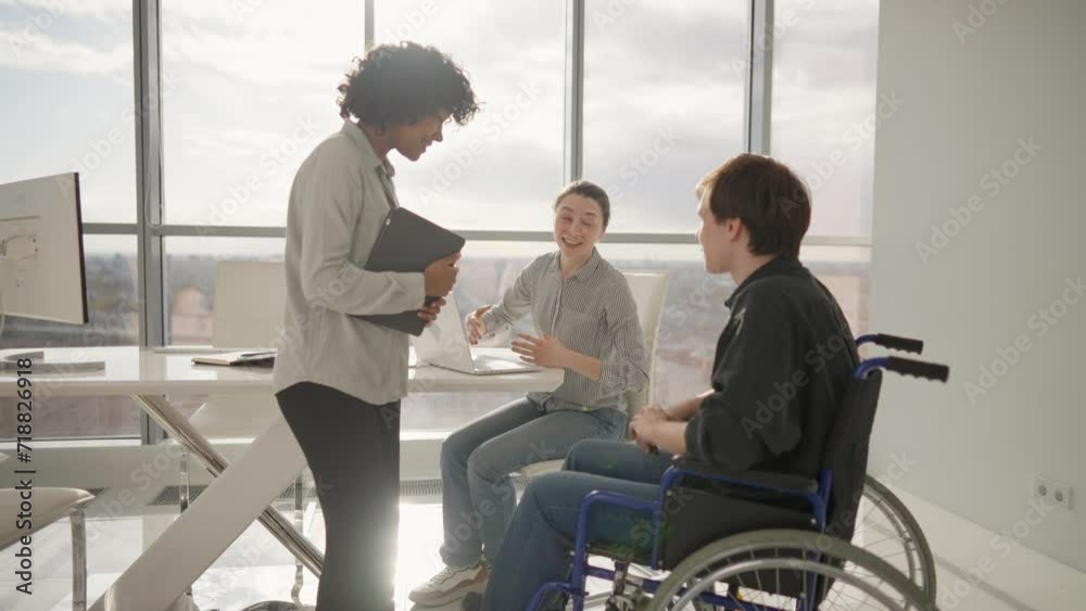 Colleagues, woman shows to man in wheelchair pie chart on paper document work together in office. Workers discuss analytics data. Usual life of people with physical disability, teamwork concept. Colleagues, woman shows to man in wheelchair pie chart on paper document work together in office. Workers discuss analytics data. Usual life of people with physical disability, teamwork concept.