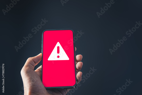 Businessman holding mobile phone with red warning alert system hacked screen. System alert for virus,spam,scam and phishing. Cyber security, data security system concept.