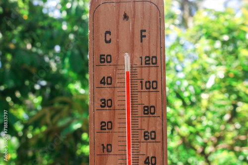 Celsius and fahrenheit scale thermometer shows plus 30 degrees during midday in Asia with trees in the background. The thermometer shows temperatures above 40 degrees in summer photo