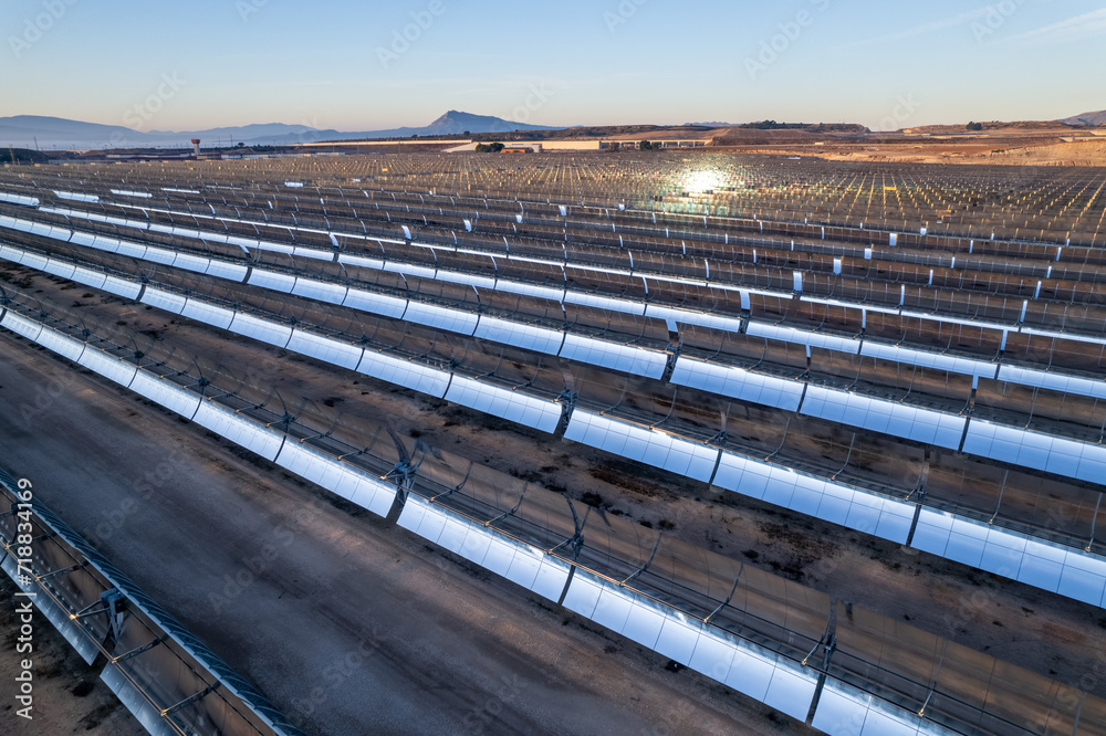 Solar thermal power plant at sunrise. Mirrors reflecting the sun, heating the water flowing through a metallic tube passing through a turbine that converts steam into electricity. Aerial photo