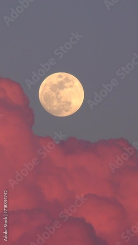 Full moon rising behind clouds illuminated by the sunset