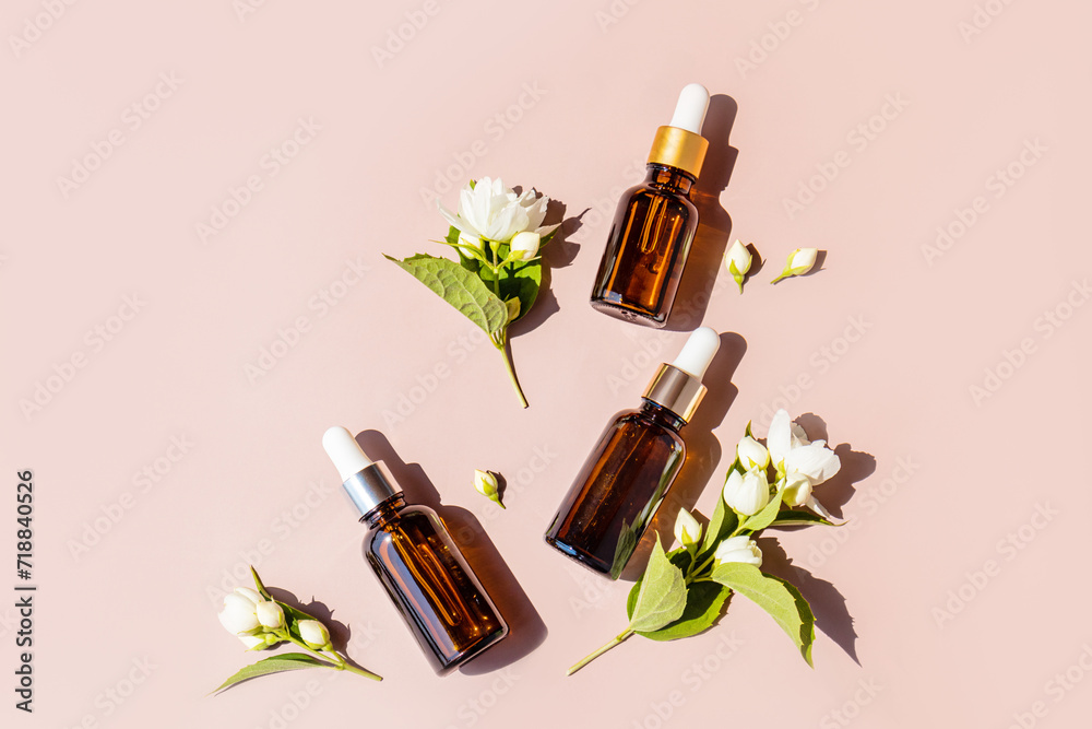 Three cosmetic bottles with a dropper lie on a pastel background between flowers and sprigs of jasmine. sunlight. Natural cosmetics. Organic care. Three cosmetic bottles with a dropper lie on a pastel background between flowers and sprigs of jasmine. sunlight. Natural cosmetics. Organic care.