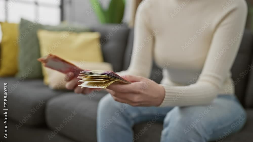 A young woman counts philippine pesos in a cozy, modern living room, creating a scene of domestic financial management.