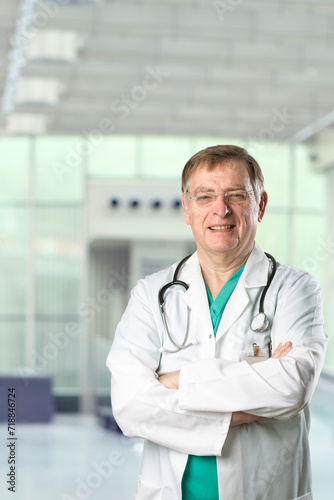 Portrait of a mature male Caucasian doctor. He is wearing a green Scrubs and a white lab coat with a stethoscope around his neck.