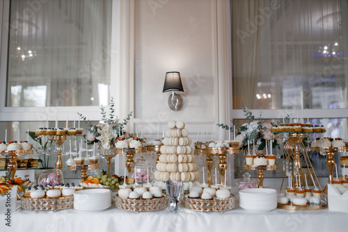 A luxurious candy bar, a festive table with sweets, macaroons, cakes and a cake. Front view. General plan.
