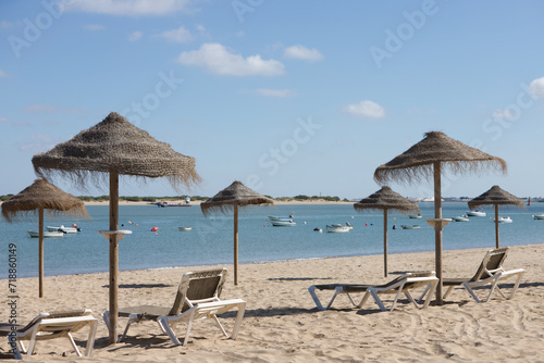 Straw umbrellas and sun loungers on the beach on a sunny day. The concept of rest and relaxation  holidays and travel. In the background the fishermen s boats.