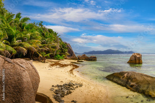 Anse Source D'argent beach at the La Digue Island, Seychelles, with calm water of the Indian Ocean, amazing granite rock formations, palm trees and mountains in the background.