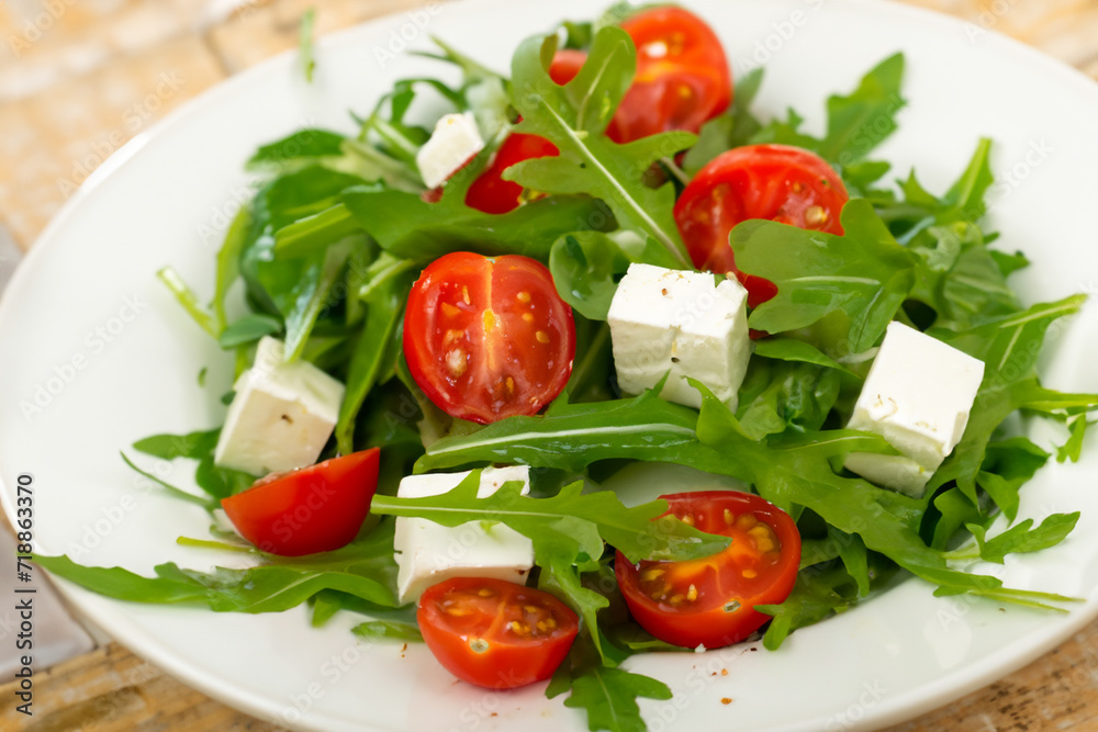women's salad. on a white plate lie arugula leaves, halves of small tomatoes and cubes of feta cheese, healthy food concept women's salad. on a white plate lie arugula leaves, halves of small tomatoes and cubes of feta cheese, healthy food concept