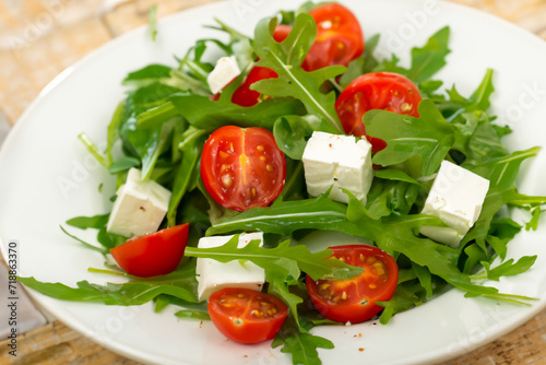 women's salad. on a white plate lie arugula leaves, halves of small tomatoes and cubes of feta cheese, healthy food concept